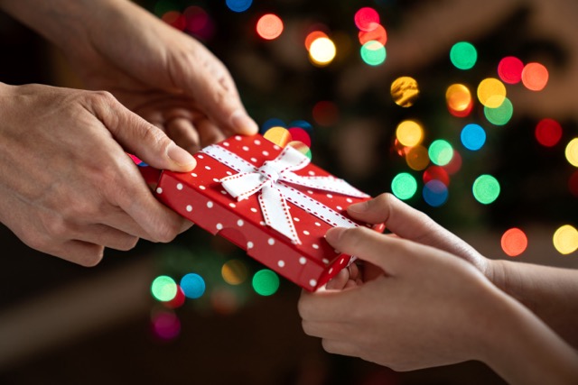 Parent giving child a red Christmas gift box with white ribbon